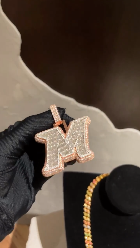 Angled view of the M letter pendant, capturing the shine of its round and baguette-cut diamonds